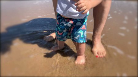 Téléchargez les photos : Enfant au bord de la plage pour la première fois. Bébé bébé sentir l'eau - en image libre de droit
