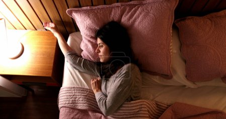 Téléchargez les photos : Woman switches nightstand lamp light on and gets out of bed in the night - en image libre de droit
