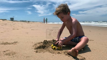 Téléchargez les photos : Petit garçon jouant au château de construction de plage avec du sable - en image libre de droit