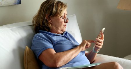 Foto de Candid older woman using cellphone device. Senior person reading content on phone - Imagen libre de derechos
