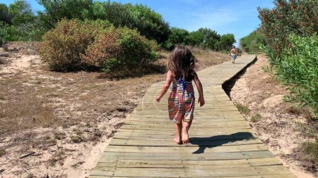 Téléchargez les photos : Little girl child running towards beach or wooden pathway - en image libre de droit