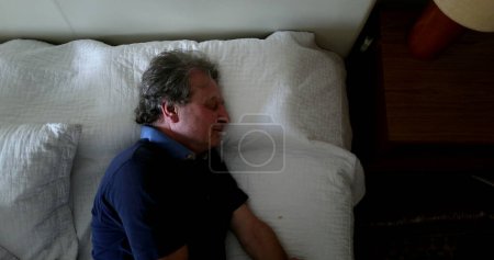 Photo for Old man lies down in bed for nap time - Royalty Free Image