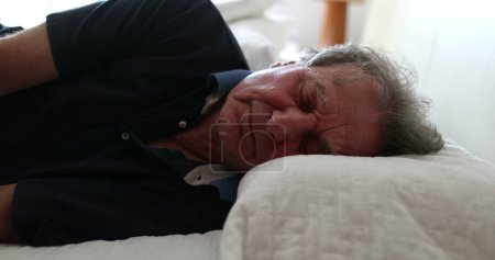Foto de Old man lays down in bed to nap. Senior guy resting napping - Imagen libre de derechos