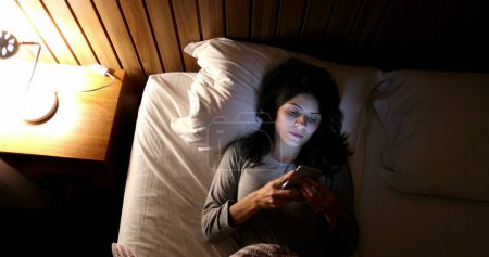 Téléchargez les photos : Woman lying in bed picks up cellphone and turns on screen before sleep - en image libre de droit