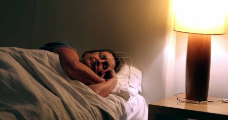 Téléchargez les photos : Woman in 60s sleeping in bed at night, turns off nightstand light - en image libre de droit