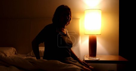 Photo for Woman sitting on the side of th ebed preparing to go to sleep - Royalty Free Image