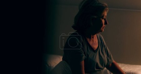 Téléchargez les photos : Senior woman getting up from bed at night. Tired person waking up at dawn - en image libre de droit