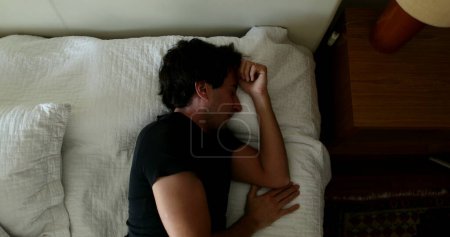 Téléchargez les photos : Young man lying down in bed falling asleep in afternoon nap - en image libre de droit