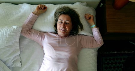 Foto de Woman lies down in bed to rest and take nap - Imagen libre de derechos