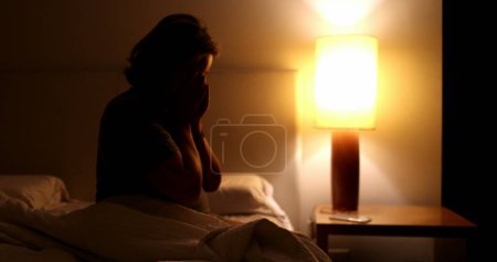 Photo for Worried older woman sitting by the side of bed at night unable to sleep suffering from anxiety - Royalty Free Image