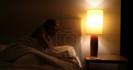 Foto de Sleepless Older woman turns light ON suffering from insomnia - Imagen libre de derechos