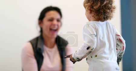 Foto de Baby toddler covered in paint, artistic cute infant interaction with mother - Imagen libre de derechos