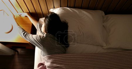 Téléchargez les photos : Woman in bed turning nightstand light OFF - en image libre de droit