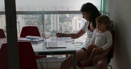 Téléchargez les photos : Mother multi-tasking at home, infant toddler boy watching cartoon on laptop while mom studying - en image libre de droit
