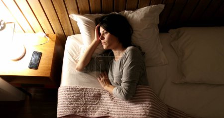 Foto de Woman suffering from insomnia turns light ON and picks up cellphone - Imagen libre de derechos
