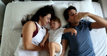 Téléchargez les photos : Cute family together in bed. Mother, father, and infant toddler boy - en image libre de droit