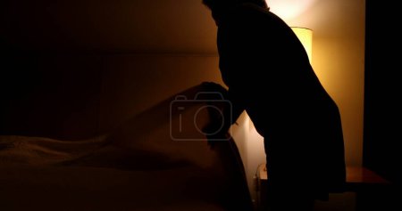 Foto de Older woman prepares to go to bed and sleep. Person lays down in bed and turns off night stand besides bed - Imagen libre de derechos