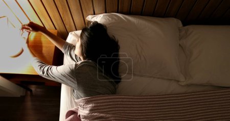 Foto de Woman in bed turning nightstand light OFF - Imagen libre de derechos