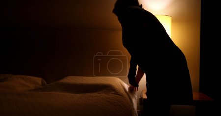 Photo for Older woman prepares to go to bed and sleep. Person lays down in bed and turns off night stand besides bed - Royalty Free Image