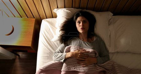 Foto de Woman lying down in bed resting and turning nightstand bed light OFF, top view - Imagen libre de derechos