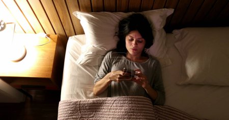 Photo for Woman suffering from insomnia turns light ON and picks up cellphone - Royalty Free Image