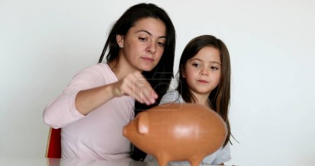 Téléchargez les photos : Mother and daughter financial savings adding coins inside piggy bank - en image libre de droit
