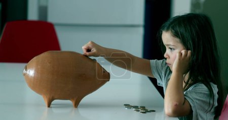 Téléchargez les photos : Child adding coins inside piggy bank - en image libre de droit