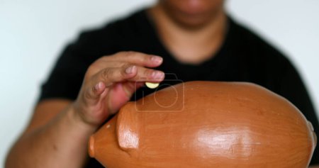 Téléchargez les photos : Black woman putting coins inside piggy bank, saving money concept - en image libre de droit