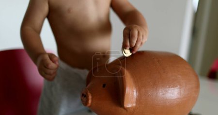 Téléchargez les photos : Child saving money adding coins inside piggy bank - en image libre de droit