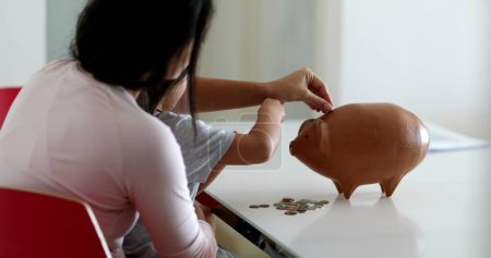 Foto de Mother and daughter financial savings adding coins inside piggy bank - Imagen libre de derechos