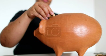 Photo for Close-up black person hands putting coins inside piggy bank - Royalty Free Image