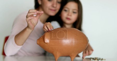 Téléchargez les photos : Mother and daughter financial savings adding coins inside piggy bank - en image libre de droit
