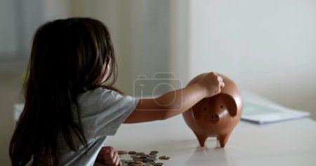 Photo for Little girl adding coins inside piggy bank. Child saving money concept - Royalty Free Image