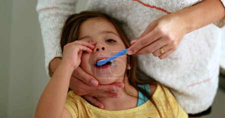 Foto de Parent brushing daughter teeth before bed. Mother brushes little girl tooth with toothbrush - Imagen libre de derechos