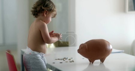 Téléchargez les photos : Adorable baby boy adding savings inside piggy bank - en image libre de droit