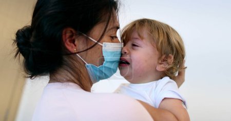 Téléchargez les photos : Tearful baby boy. Mother wearing surgical mask holding upset crying infant - en image libre de droit