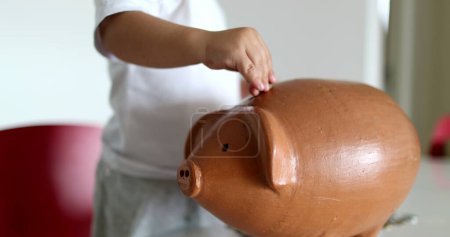 Téléchargez les photos : Baby hands putting coins inside piggy bank - en image libre de droit