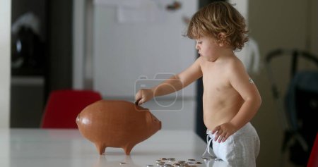 Téléchargez les photos : Child putting coins savings inside piggy bank - en image libre de droit