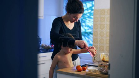 Téléchargez les photos : Mère franche et enfant cuisinent à la maison, préparent des pâtisseries ensemble dans la vraie vie parentale authentique scène domestique - en image libre de droit