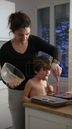 Photo for Mother and child cooking together standing at kitchen. Mom preparing cakes with small boy. Vertical video - Royalty Free Image
