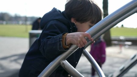 Foto de Estructura del parque infantil escalada, las manos sosteniendo en barras de metal en el exterior durante la temporada de otoño, usando chaqueta a la luz del sol - Imagen libre de derechos