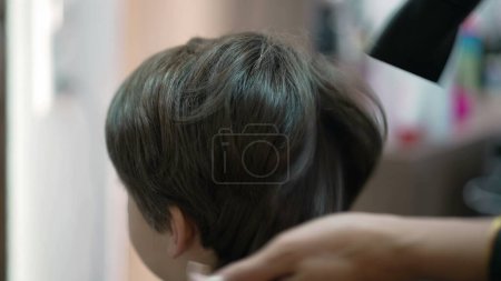 Téléchargez les photos : Coiffeur professionnel Séchage et peignage des cheveux de l'enfant au salon, Petit garçon Obtenir une coupe de cheveux - en image libre de droit