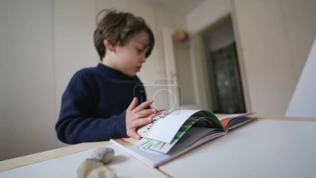 Foto de Niño pasando páginas de libros mirando imágenes y texto. Niño leyendo material de la escuela de jardín de infantes - Imagen libre de derechos