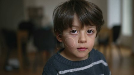Téléchargez les photos : Portrait d'un garçon de 4 ans en gros plan regardant la caméra avec une expression neutre à l'intérieur - en image libre de droit