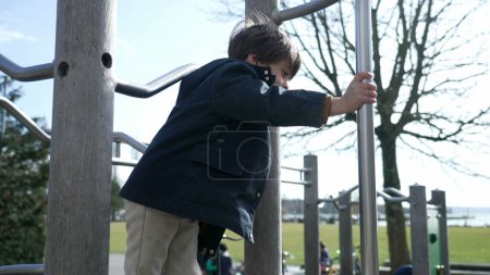 Photo for Active small boy sliding down metal bar at playground during fall season, child wearing jacket and boots playing outdoors - Royalty Free Image