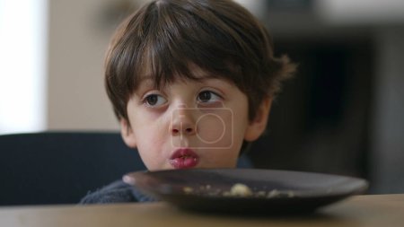 Photo for Contemplative close-up child's face lost in thought while chewing food, small boy gazing in the distance in deep mental reflection while eating - Royalty Free Image