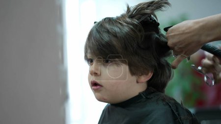 Téléchargez les photos : Petit garçon se faire couper les cheveux au salon de coiffure, coiffeur professionnel cheveux d'enfant, première fois expérience - en image libre de droit