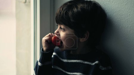 Photo for Youngster Absorbed in View, Biting into Fresh Strawberry - Royalty Free Image