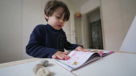 Téléchargez les photos : Enfant tournant des pages de livres en regardant des images et du texte. Petit garçon lecture maternelle matériel scolaire - en image libre de droit