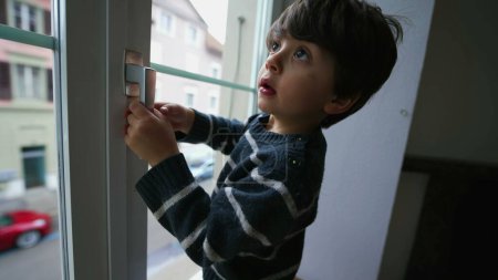 Foto de Niño sosteniendo la perilla de la ventana. Peligro concepto de niño pequeño cerca de vidrio de la residencia de apartamentos del segundo piso - Imagen libre de derechos